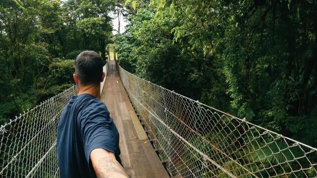 Young man filming himself with a selfie stick while walking on a suspension bridge. Personal perspective of an explorer in a Costa Rica jungle