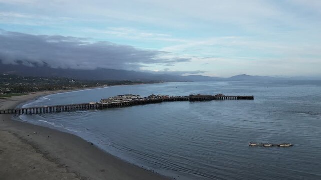 Drone shot moving forward over a beach on a rainy dusk early evening in Santa Barbara, California. Wet sand from the recent rains, approaching Stearns Wharf.