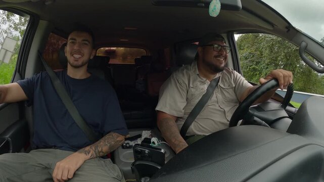 Male tour guide driving a car and talking with a young tattooed tourist during an excursion in Arenal Volcano National Park, Costa Rica