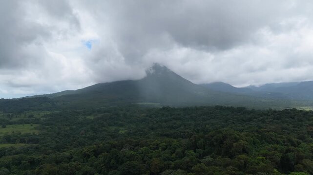 Majestic aerial view of the active Arenal Volcano in Costa Rica. Dramatic clouds moving over the peak with localized rain falling on the lush jungle
