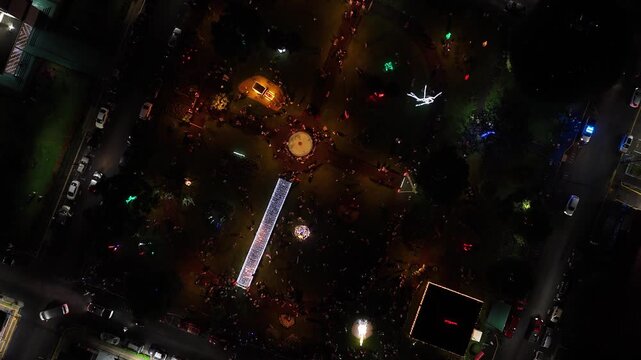 Aerial top down view of a drone flying over a crowded park. Bright Christmas lights and decorations illuminating the night in La Fortuna