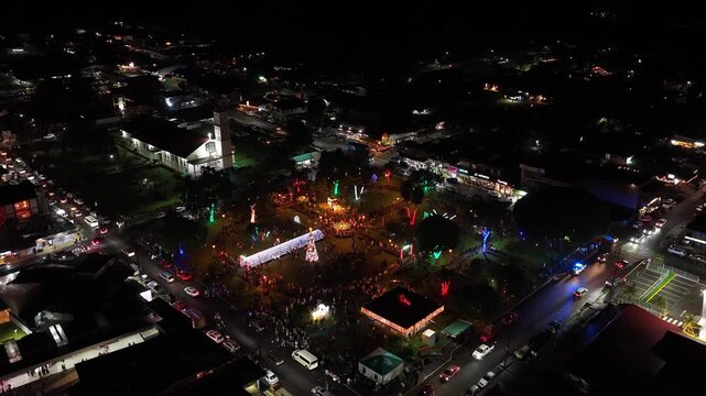 Night aerial shot of a town square in La Fortuna, Costa Rica, decorated for Christmas. People gathering in the illuminated park for festivities