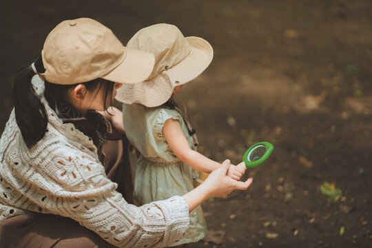 Mother and toddler daughter exploring nature together with magnifying glass outdoors, encouraging curiosity, discovery, observation, hands-on learning, childhood development