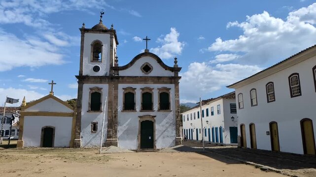 Static slow motion shot of the iconic Santa Rita Church built in 1722 in Paraty, Brazil, with whitewashed colonial architecture and blue sky.