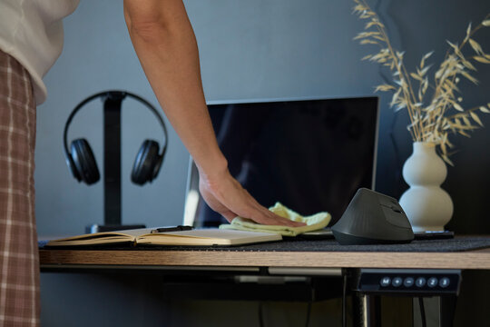 Person wiping wooden desk with cloth beside monitor, mouse, headphones and notebook