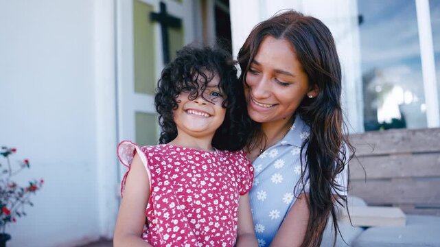 Portrait of a beautiful smiling latin mother holding her lovely daughter on the porch. Happy family moment outdoors on a sunny day