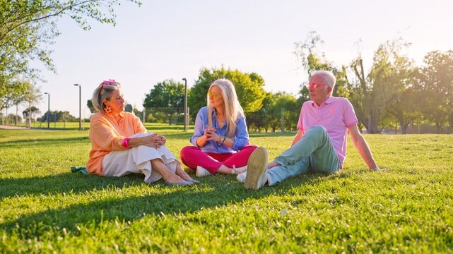 Group of stylish seniors sitting on grass, talking and enjoying sunny day