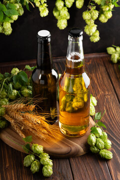 Two bottles of beer with fresh hops and wheat ears on a wooden table