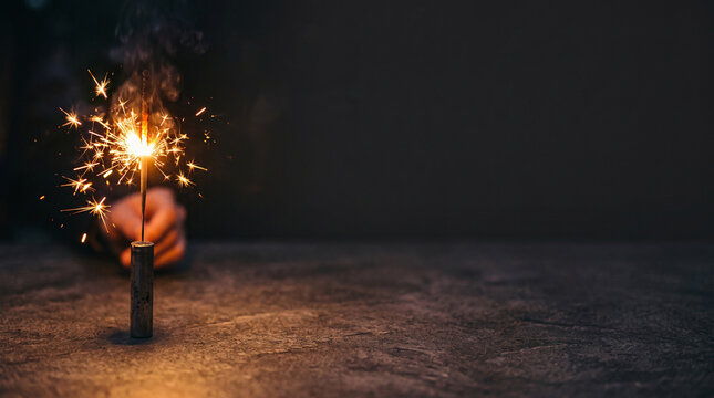Single burning sparkler creating bright golden lights on a dark rustic textured tabletop for Diwali.