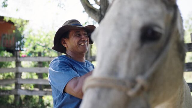 Smiling latin cowboy petting and grooming his white horse on a sunny day. A lovely moment showing the bond between a man and his animal