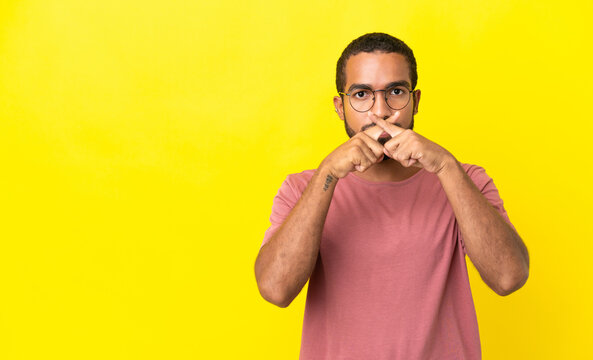 Young latin man isolated on yellow background showing a sign of silence gesture