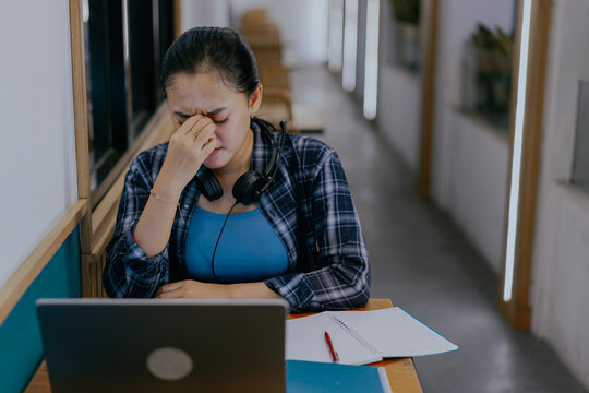 Tired young Asian woman feel pain eyestrain rubbing dry irritated eyes fatigued from computer work. Stressed female suffer from headache bad vision sight problem sit at home table and using laptop.