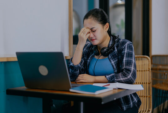 Tired young Asian woman feel pain eyestrain rubbing dry irritated eyes fatigued from computer work. Stressed female suffer from headache bad vision sight problem sit at home table and using laptop.