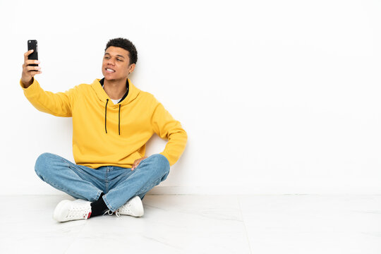 Young African American man sitting on the floor isolated on white background making a selfie
