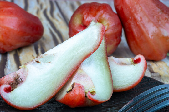 Fresh red wax apples, whole and sliced, presented on a black plate with studio lighting.