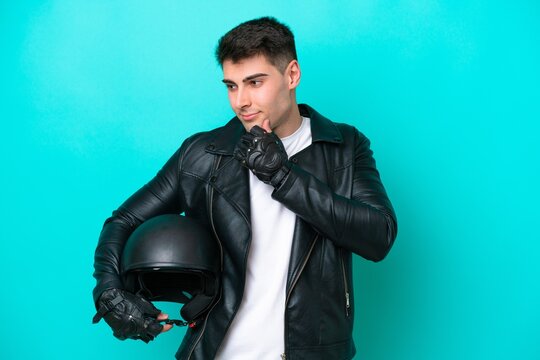 Young caucasian man with a motorcycle helmet isolated on blue background looking to the side and smiling