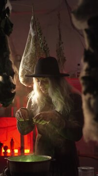  witch stands in her home, surrounded by cobwebs and bundles of dried herbs, preparing a poison or a love potion she chants a spell and tosses dried herbs into a cauldron of bubbling green liquid.