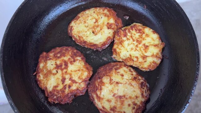 Four golden brown potato pancakes frying in cast iron pan, crispy latkes cooking in oil, traditional fried food, draniki