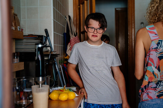 Teenage boy with Down syndrome standing in family kitchen during everyday food preparation at home