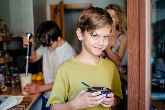 Young boy holding bowl while brother with Down syndrome prepares food in busy family kitchen at home