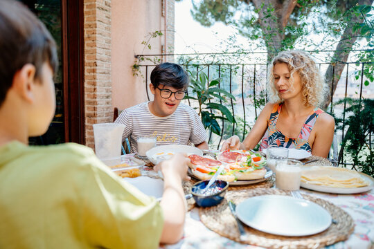 Family breakfast with mother and two sons including teenage boy with Down syndrome on sunny terrace