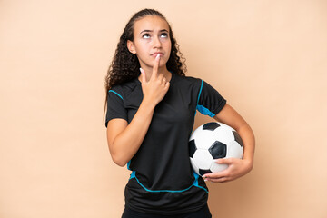 Young football player woman isolated on beige background having doubts while looking up © luismolinero