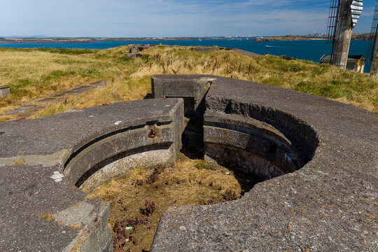 Circular concrete gun emplacement at coastal battery, looking out over grass headland and blue sea waters towards distant coast, West Blockhouse, Wales