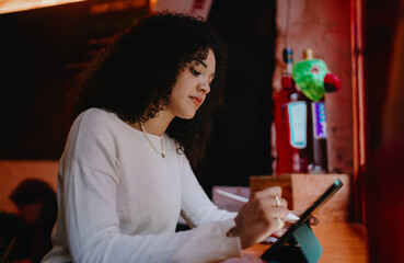 Concentrated young woman with curly hair using digital tablet and stylus pencil tool in creative studio, focused female freelancer working remotely on web design project, side view © BullRun