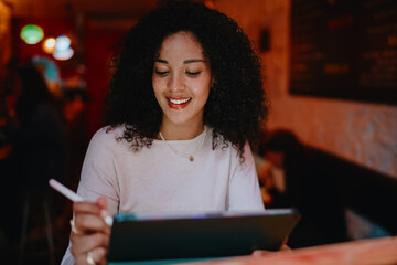 Smiling young woman using touch screen digital tablet and writing with stylus pen tool in creative space, female student e-learning online or working on project design concept portrait © BullRun