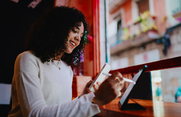 Happy young woman typing on smartphone screen while drawing with stylus pen on digital tablet in modern cafe, female student multitasking with mobile technology concept portrait © BullRun