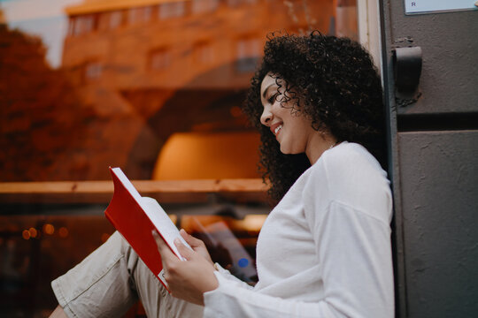 Smiling young woman in round eyeglasses scrolling social media on smartphone screen near illuminated bar shelves in night club, modern digital communication and connection concept