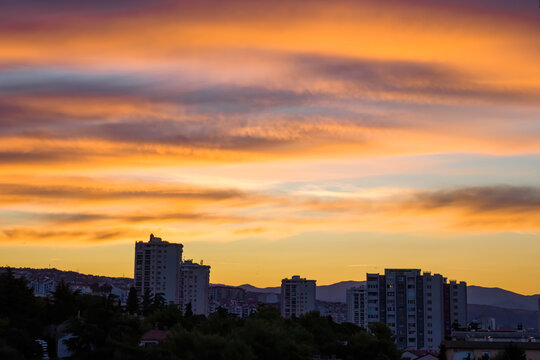 Panoramic urban view of Rijeka, Croatia, at sunset, with residential high-rise buildings silhouetted against the dramatic Kvarner Bay landscape and distant mountains