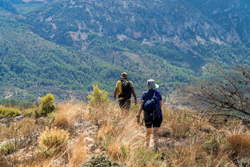 Obraz premium Two hikers walking on arid landscape with mountains on a summer day with sun and clouds