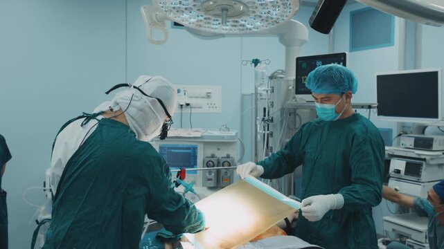 Surgical team places a sterile drape over a patient to create the sterile field before an operation. Preoperative preparation, infection control, patient safety, hospital procedure and clinical educat