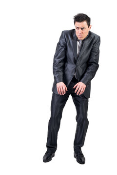 Full body of scared man in elegant formal suit standing with raised shoulders in light studio