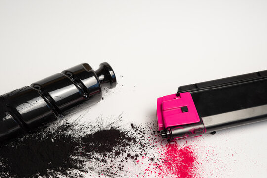 Black and magenta toner cartridges with spilled toner powder on white background and copy space