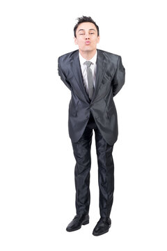 Full body of positive young guy with dark hair in elegant suit pouting lips and looking at camera while leaning forward with hands behind back