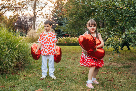 Children Play With Red Heart-Shaped Balloons in a Garden During Summer