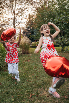 Children Celebrate Summer Outdoors With Red Heart Balloons While Playing in the Park During a Holiday