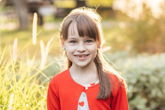 Girl Smiles in Summer Sunlight With Heart Decorations on Her Shirt During a Holiday Celebration in a Park Setting