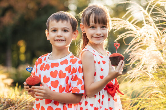 Children Enjoy Summer Holiday With Red Heart-Themed Clothing While Holding Cupcakes in a Sunny Outdoor Setting
