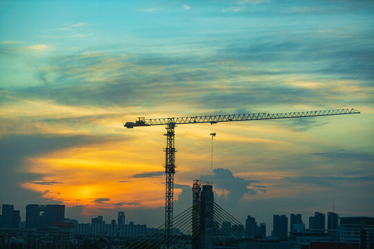 Towering construction crane silhouetted against a vibrant sunset sky over city
