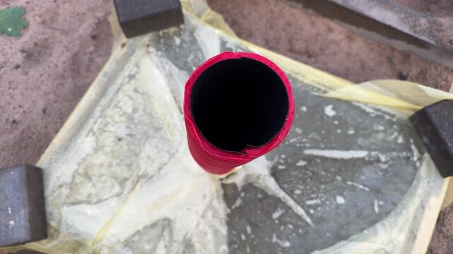 Red plastic pipe tube top view on plastic sheet outdoors, black interior visible, construction or plumbing work site, industrial materials