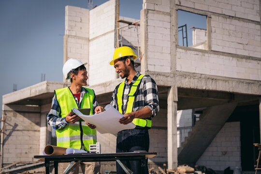 Two Asian Construction Workers Reviewing Plans on Site Young Adu