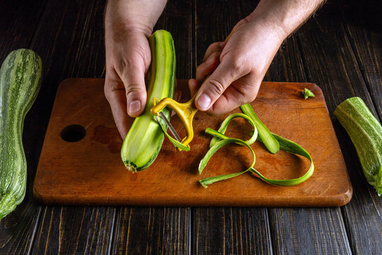 Hands skillfully peel a vibrant green zucchini on a warm wooden cutting board, showcasing the energy of cooking in a cozy kitchen. Fresh peels curl away, hinting at a delicious meal