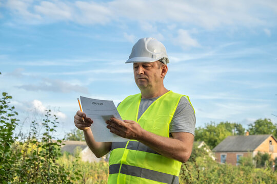 A construction worker stands outside, wearing a safety helmet and a fluorescent vest, reviewing project documents