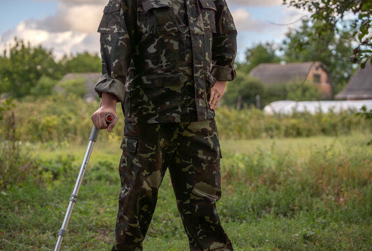 A soldier in camouflage attire stands tall in a vibrant green field, embodying strength and determination despite using a crutch for support