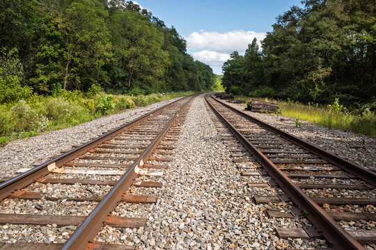 Twin railroad tracks curving through lush Pittsburgh woodlands under summer sky