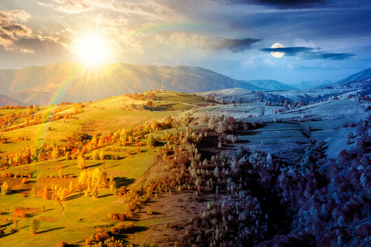 countryside landscape in autumn. day meet night. sun and moon over rural scenery in Carpathian mountains. colorful deciduous forest by the rural fields on a hillside under epic sky