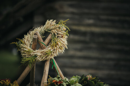 Decorative floral wreath made of dried grasses and herbs displayed on a wooden stand against a rustic wooden background in a natural outdoor setting